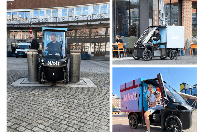 A three-image collage showing a black Wolt-branded CityQ four-wheel cargo e-bike in a city setting, including a front view between bollards, a side view outside a café, and a rider seated in the vehicle with the side door open.